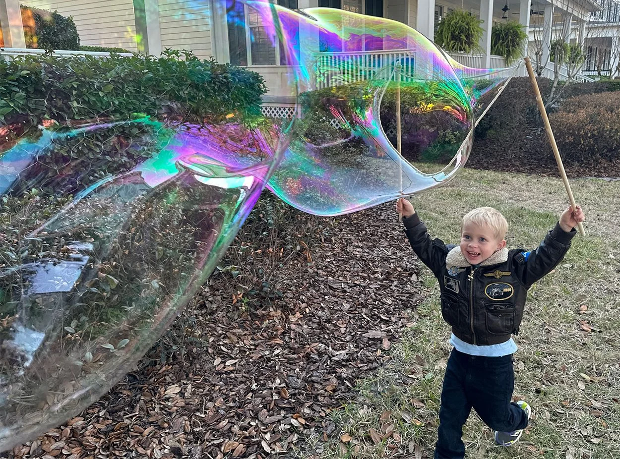 A smiling young boy raising his BubbleStix to make a giant rainbow bubble